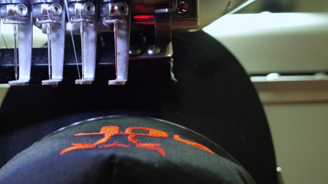 Machine embroidery of a black hat. Embroidering a cow's head with red thread shot close-up. Concept of: Automated work, Embroidery machine, Thread, Fabric, Needle, Hat. 4k video 50fps.