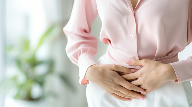 An Asian woman in casual clothing bent over slightly, suffering from stomach cramps. Focused details on her expression and posture.