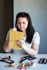 Vertical image of Millennial Caucasian woman doing self make up applying concealer on face with...