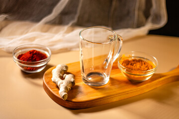 Empty transparent cup on wooden tray with turmeric and chili species. Mock up for design. Served table. Preparation for making drink