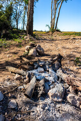 Remnants of a campfire in a rural setting, featuring charred logs and scattered stones