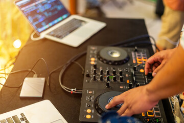 DJ at Work: The hands of a skilled DJ are expertly manipulating the controls of a mixing console, crafting music and rhythms for an unseen audience, with a laptop nearby and a hard drive ready.