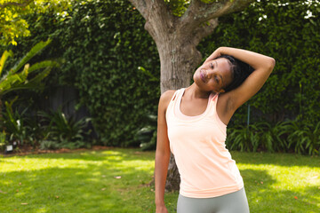 Woman stretching neck in sunny garden, enjoying outdoor exercise and relaxation, copy space