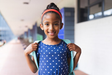 Smiling girl with backpack standing in school hallway, ready for class