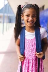 Smiling girl with backpack standing in school hallway, ready for class