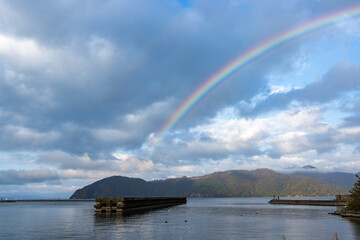 山に囲まれた静かな湖の上に架かる虹と雲空