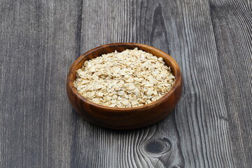 Oat flakes uncooked in a brown bowl on wooden table. Healthy food for breakfast