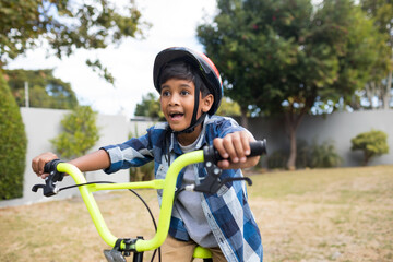 Fototapeta premium Excited boy riding bicycle in backyard, wearing helmet and enjoying outdoor fun, copy space