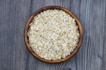 Oat flakes uncooked in a brown bowl on wooden table. Healthy food for breakfast