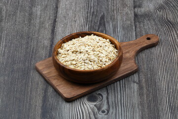 Oat flakes uncooked in a brown bowl on wooden table. Healthy food for breakfast