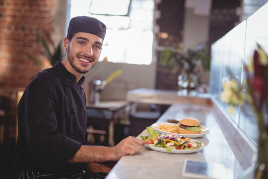 Smiling chef presenting delicious salad and burger at modern cafe counter, copy space