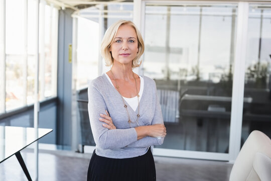 Confident businesswoman standing in modern office, arms crossed, looking determined