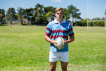 Holding rugby ball, athlete wearing striped jersey on field, looking determined, copy space