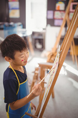 Obraz premium Asian boy painting on easel in art class, enjoying creative activity at school, copy space