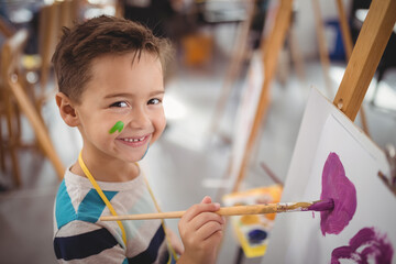 Smiling boy painting on easel in school art class, enjoying creativity