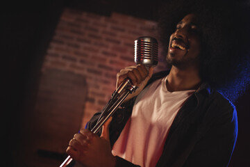 Musician passionately singing into vintage microphone on stage in dimly lit venue, copy space
