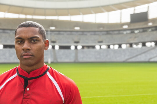 Rugby player in red jersey standing confidently in empty stadium, copy space