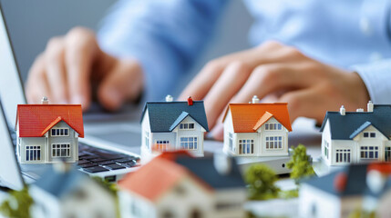 Real estate agent working on laptop with miniature houses, showcasing property listings and market analysis