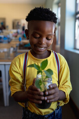 Smiling boy in school holding plant in jar, learning about nature