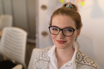 Smiling woman with glasses in office, looking confidently at camera