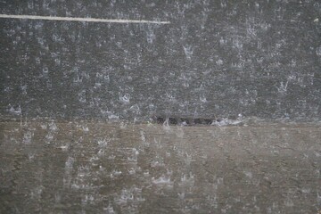 heavy rain falls on the road and runs into a drain at the roadside