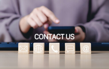 Contact Us and customer support concept. A person using a smartphone with wooden blocks contact icons, email, phone, chat, and web represents customer service, communication, and support assistance.