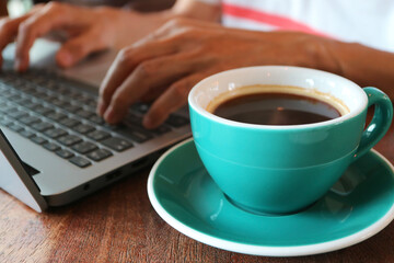 Closeup of a cup of coffee with a man working on laptop in the background