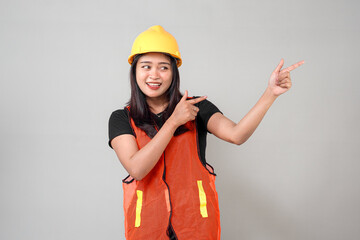 Cheerful Asian female construction worker wearing a yellow hard hat and orange safety vest, smiling...