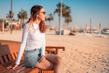 Tourist relaxing on a bench at public beach, enjoying the stunning sunset views over the Arabian Gulf in UAE