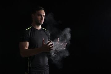 Man clapping hands with talcum powder before training on black background. Space for text