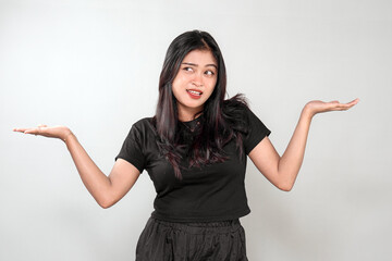 An Indonesian woman in a black outfit makes a playful, uncertain expression with a shrug. She...