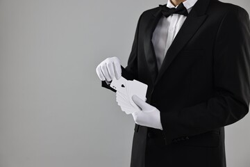 Illusionist taking one playing card from deck on grey background, closeup. Space for text