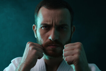 Karate fighter wearing uniform in color lights and smoke, closeup