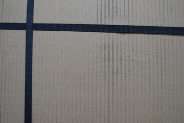 Fototapeta premium A cardboard box with a black tape running across it. The box is brown and has a cross pattern on it