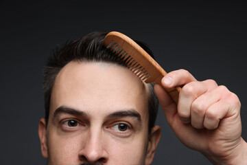 Handsome man combing his hair on dark background, closeup