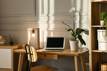 Comfortable workplace with modern laptop and lamp on wooden desk in home office