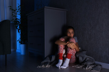 Scared girl hiding behind chest of drawers in her room at night
