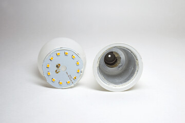 LED bulb disassembled. LED fix plate with small lighting diodes in circle, near to rim, plastic housing with aluminum thermal transfer heat sink inside, plastic white diffuser