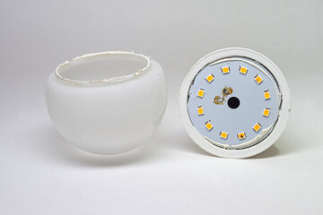 LED bulb disassembled. removed domed white translucent light dispersion optics with silicon sealant at narrow rim. showing inner metal, blue film coated plate with mounted light emitting LEDs array