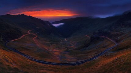 Fototapeta premium Dramatic sunset over winding mountain road in valley.