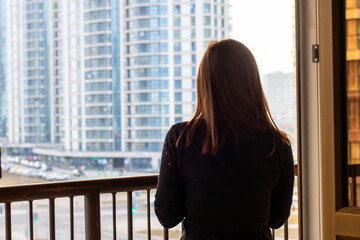 A woman is standing on a balcony gazing out at the sprawling cityscape
