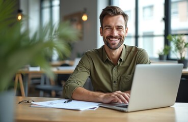 Obraz premium Caucasian IT pro works on laptop in office. Businessman poses at desktop, types on computer looking at camera. Smiling man works, develops new digital tech, app for marketing, online service.