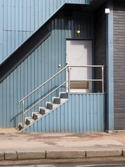 In the center of the building, there are stairs with metal railings leading to a white door. The...