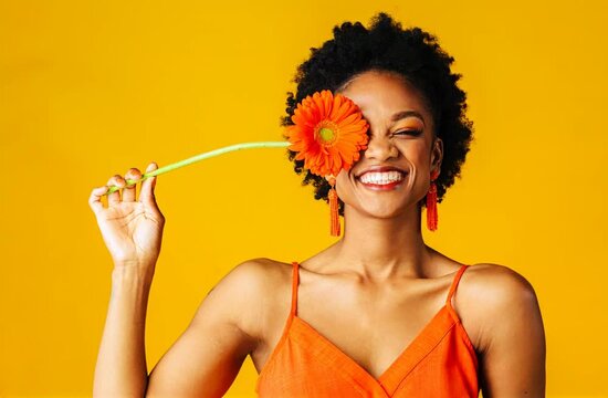 happy young woman holding an orange Gerbera daisy covering her eye