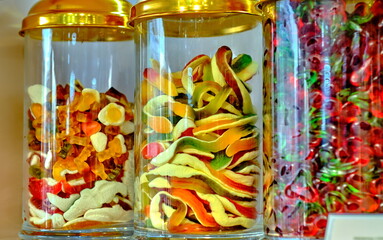 Various sweets: candies, lollipops, gummy worms, in a glass jar with a golden lid on the counter in a candy store.