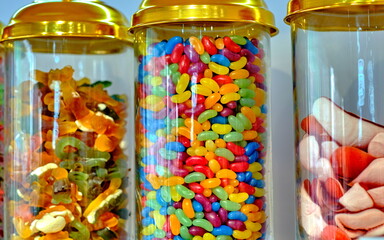 Various sweets: candies, lollipops, gummy worms, in a glass jar with a golden lid on the counter in...