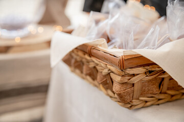 A rustic woven basket with a beige cloth holds individually wrapped treats, sitting on a table with soft lighting. The warm tones and delicate details create a cozy and inviting atmosphere.