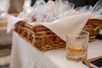 A rustic basket with neatly wrapped treats and a textured glass with a golden drink rest on a linen-covered table, evoking a cozy, artisanal setting with warmth, simplicity, and hospitality.