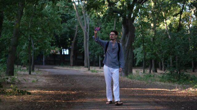 Young man blogger walks in the park on a sunny summer morning recording vlogs