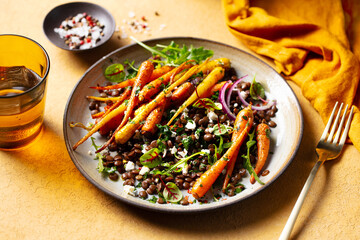 Warm salad. Roasted carrots with lentil, arugula and feta cheese. Yellow background. Close up.
